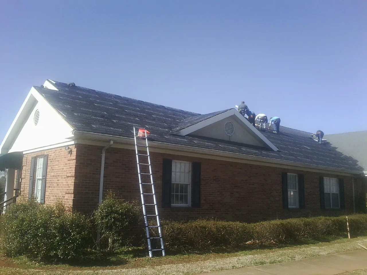 Crew tearing shingles off a brick ranch roof with a ladder set — Metal Roof Repair work by our crew in New Britain