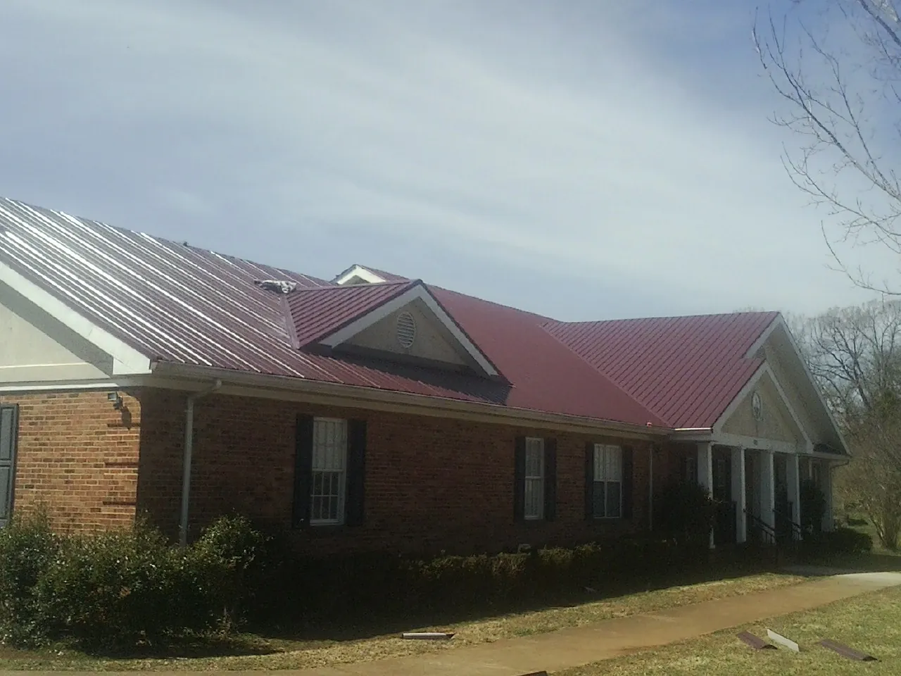Red metal roof with gabled entries on a long brick building, from a Hail Damage Roof Repair job in New Britain