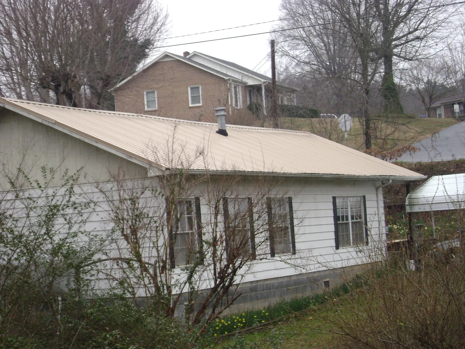 Tan metal roof on a white sided house set into a hillside — Commercial Roofing by Roofing Brothers in New Britain
